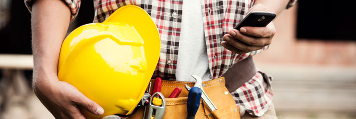 A person holding a yellow hard hat and a cell phone.